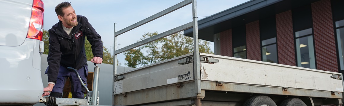man hangt aanhanger aan bestelbus