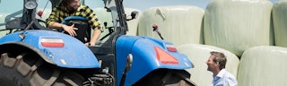 Adviseur geeft advies over agrarische bedrijfsautoverzekering aan relatie op een tractor