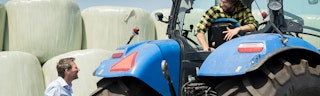 Adviseur geeft advies over agrarische rechtsbijstandverzekering aan relatie op een tractor