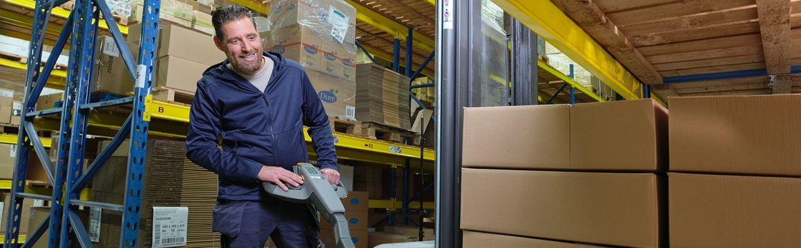 man bedient palletwagen met dozen in  magazijn
