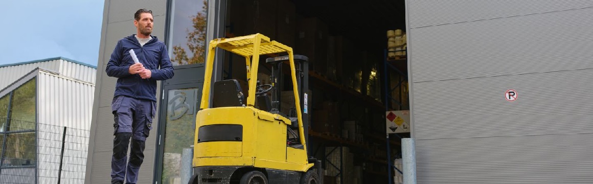 man loopt uit gebouw met gele heftruck op achtergrond